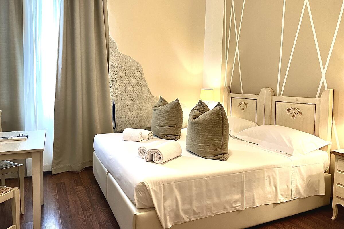A hotel room with a bed, a desk, and a large window with curtains.