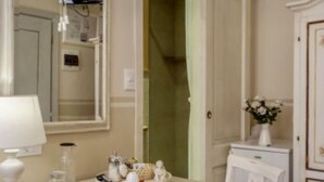 Un baño con tocador blanco, un espejo, un perchero y un pequeño jarrón con flores.
