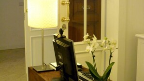 Un bureau avec un écran d’ordinateur, un clavier et une lampe. On peut y voir un vase contenant des orchidées blanches.