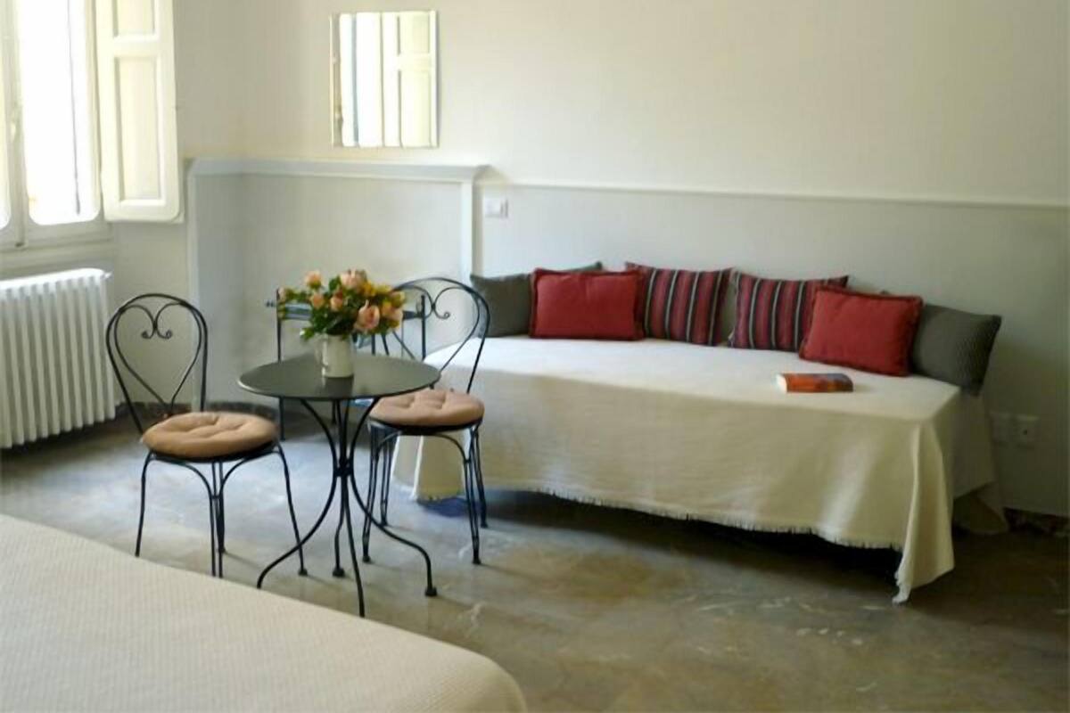 Una habitación acogedora con cama, una pequeña mesa redonda con sillas, un sofá con cojines y un radiador.