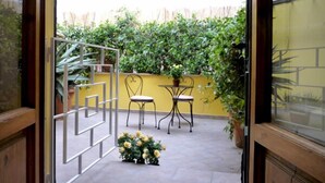 Une terrasse extérieure avec un mur jaune, deux chaises en métal, une petite table et des plantes en pot.