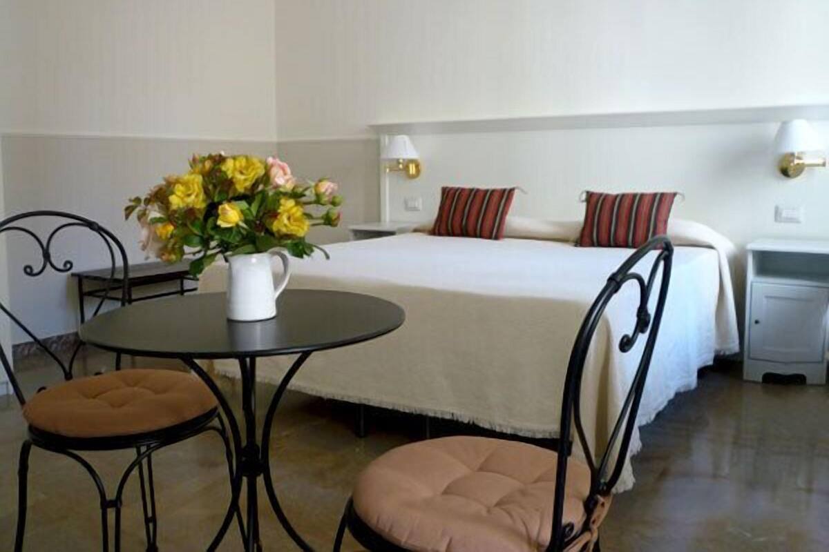Habitación de hotel con cama, mesitas de noche, una pequeña mesa redonda con un florero y dos sillas.