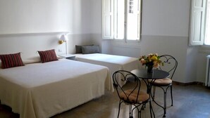 Une chambre d’hôtel avec deux lits, une petite table avec des chaises et une fenêtre avec des volets.