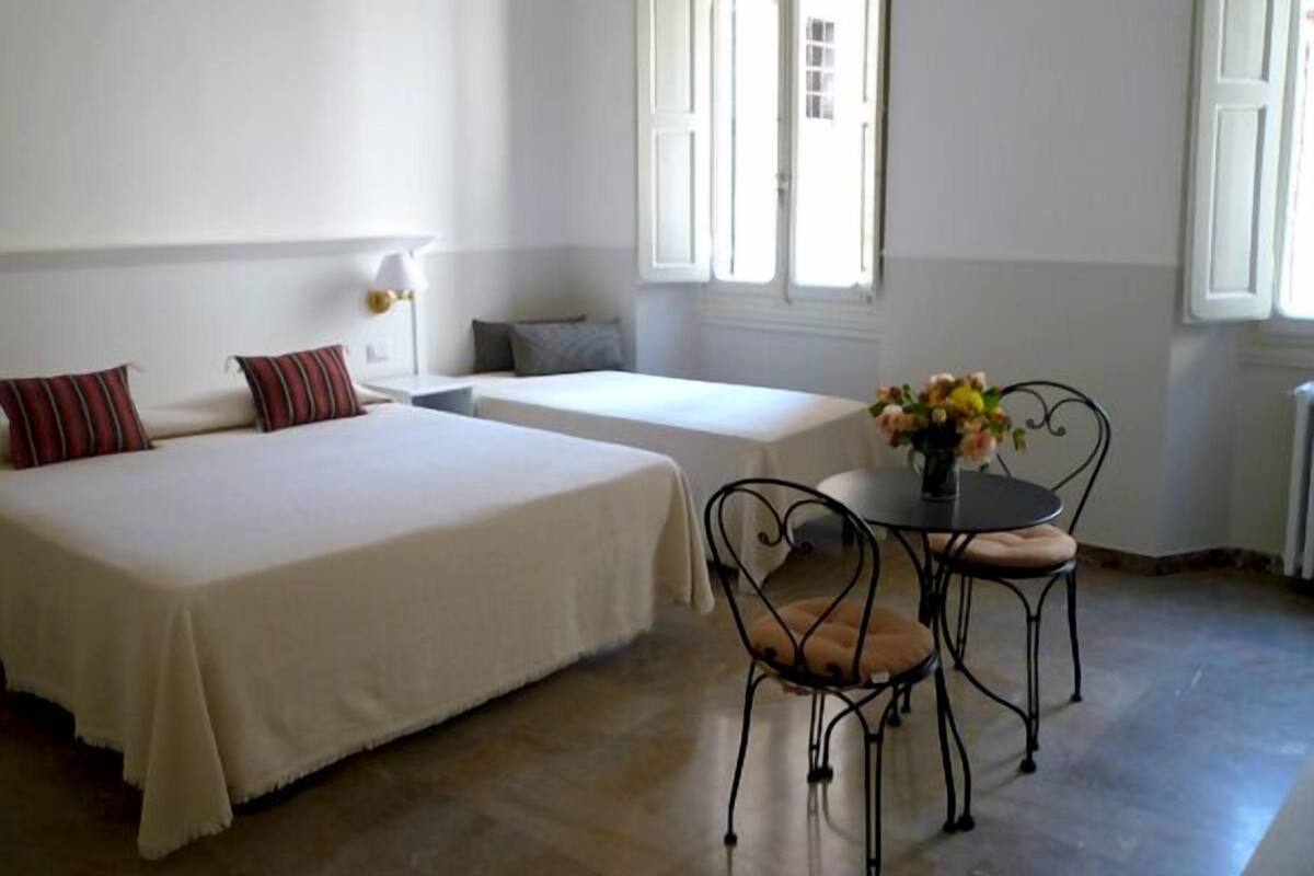 Una habitación de hotel con dos camas, una pequeña mesa con sillas y una ventana con contraventanas.