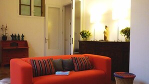 Une pièce avec un canapé rouge, un meuble en bois, une porte et une lampe fixée au mur.