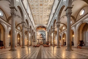 A spacious interior with high ceilings, arched columns, and a checkered floor.