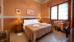 A hotel room with a bed, bedside tables, a table with a tablecloth, and a window with curtains.