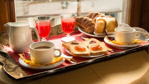 A breakfast tray with croissants, toast with jam, a glass of red juice, a cup of coffee, and a pitcher of milk.