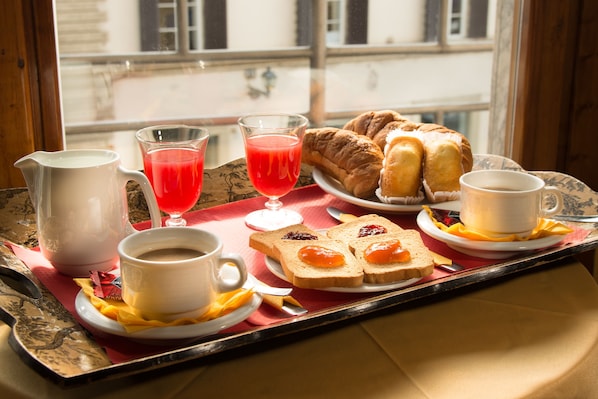 A breakfast tray with croissants, toast with jam, a glass of red juice, a cup of coffee, and a pitcher of milk.