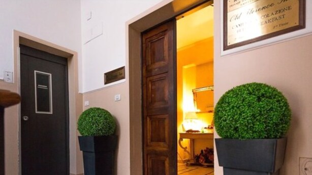A hallway with a dark wooden door, a framed sign above it, and two potted plants.