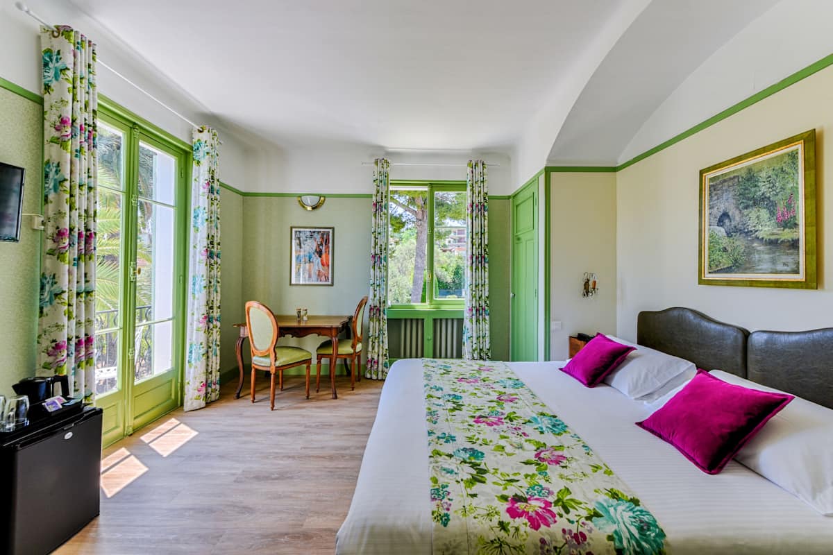A room with a bed, a desk, and a chair. There is a window with curtains.