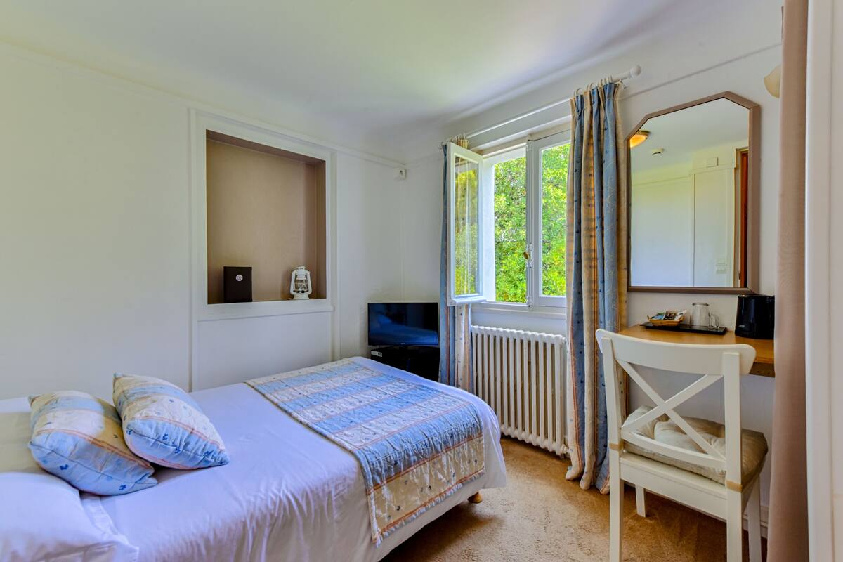 A bedroom with a bed, a desk, a chair, a TV, and a window with curtains.