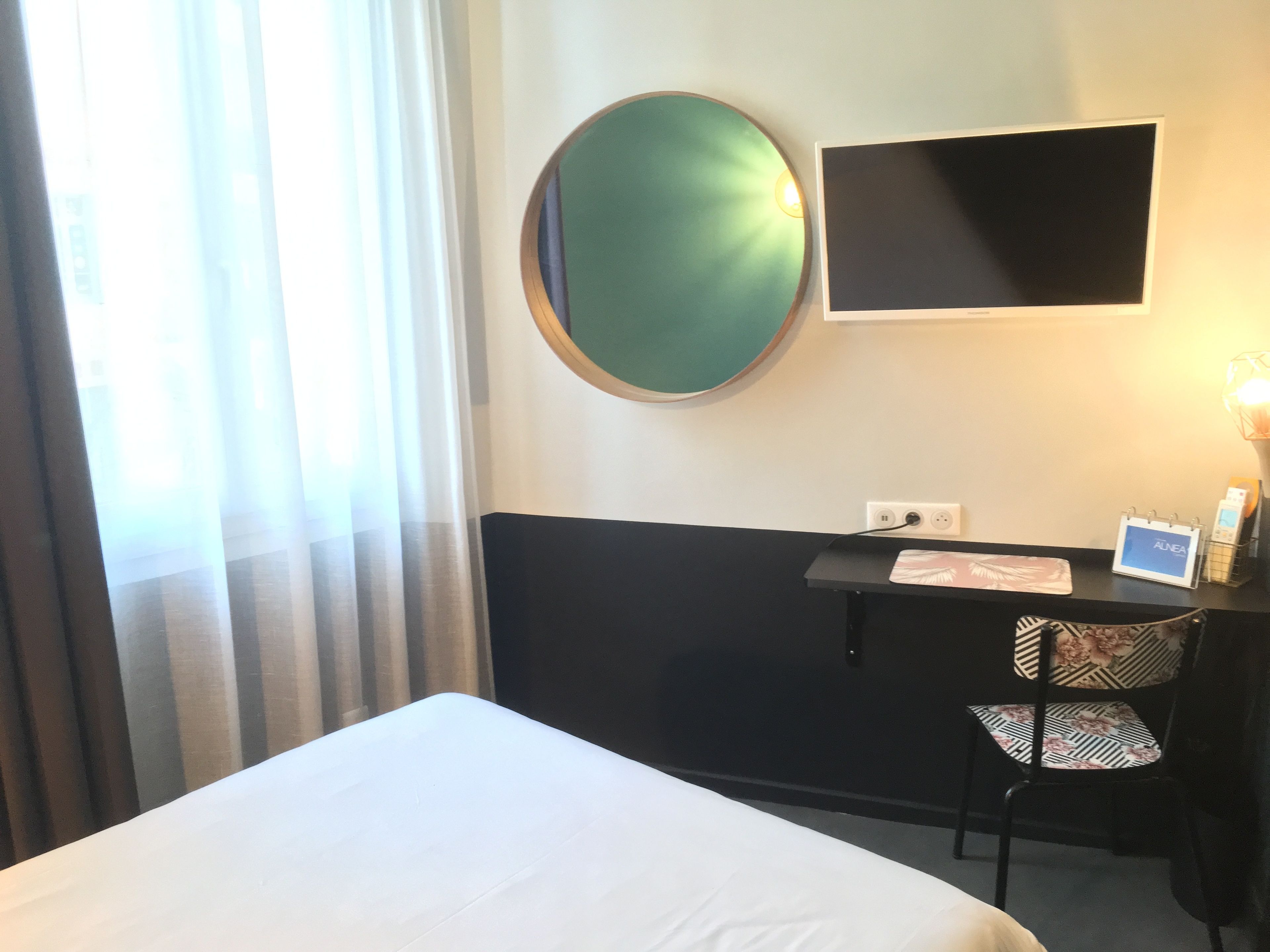 Une chambre d’hôtel équipée d’un lit, d’un bureau, d’une chaise, d’un téléviseur à écran plat et d’un miroir fixé au mur.