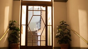 Una escalera conduce a una puerta con un diseño geométrico, flanqueada por plantas en macetas y una barandilla.