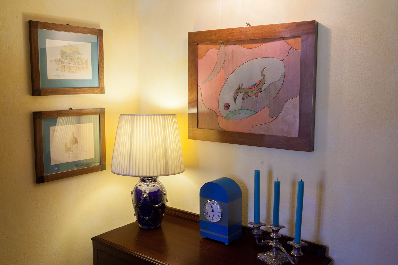 Una pared decorada con cuadros, una lámpara, un reloj y velas.