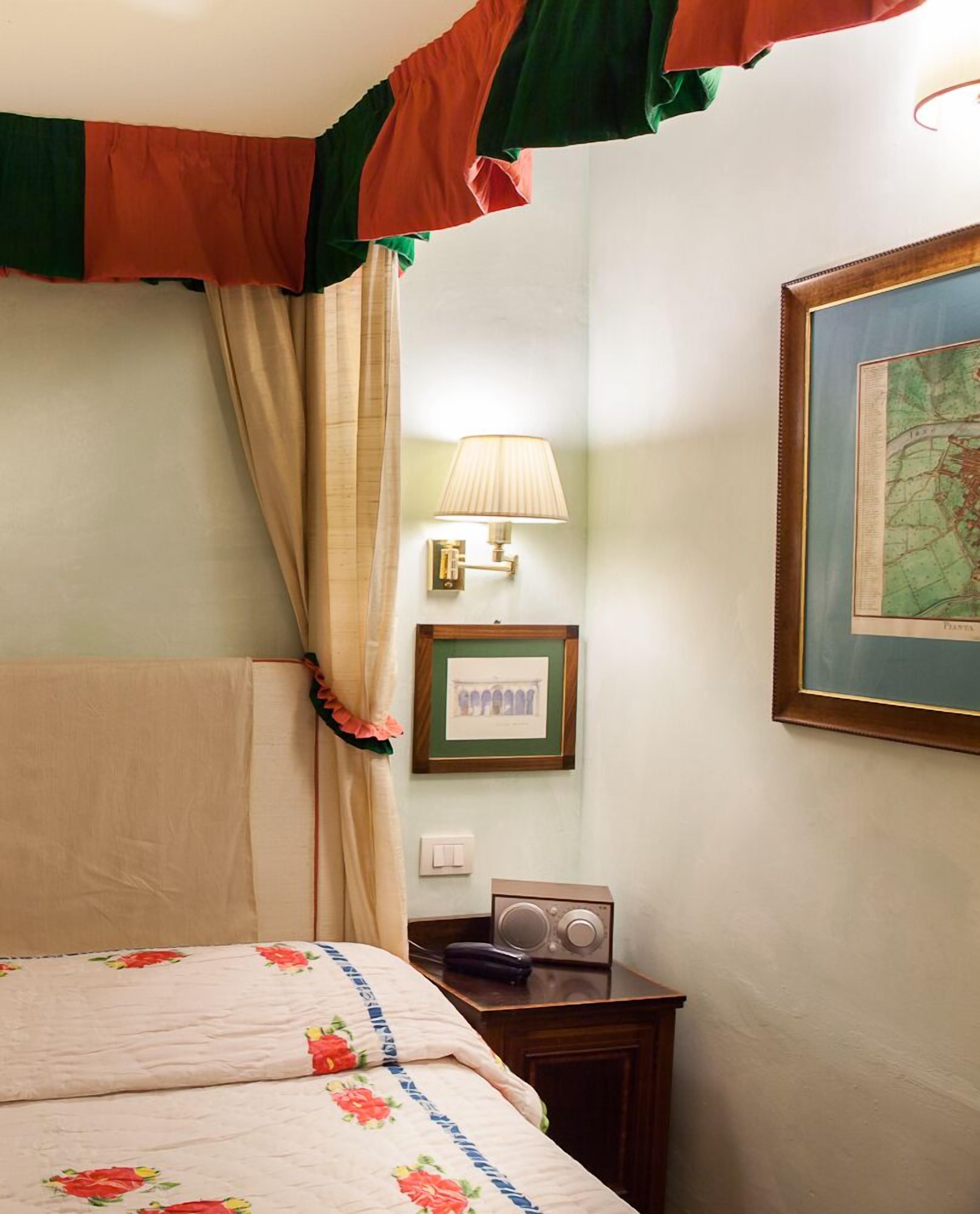 A hotel room with a bed, a lamp, a framed map, and a radio on a nightstand.