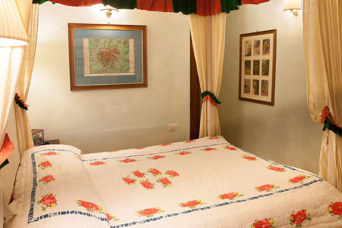 Una cama con colcha floral, un mapa enmarcado en la pared y cortinas con detalles rojos y verdes.