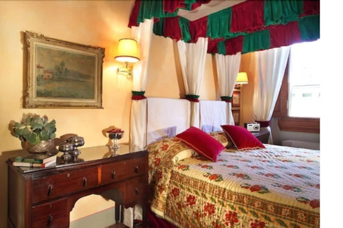 Un dormitorio con cama, mesita de noche, lámpara, cómoda y un cuadro en la pared.