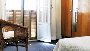 A hotel room with a wicker chair, a bed with a white bedspread, and a wooden wardrobe. - Hotel Pierre Loti (Antibes)