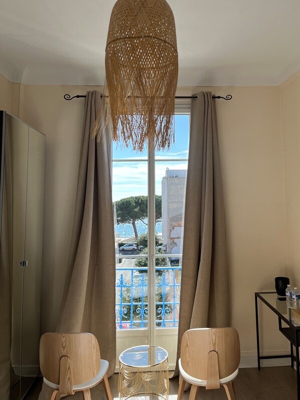 A room with a large window, two wooden chairs, a small round table, a hanging light fixture, and a view of a building and trees outside.