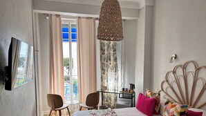 Un dormitorio con cama, dos sillas, una mesita, una lámpara colgante y vistas al exterior.