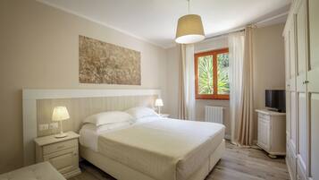 Une chambre d’hôtel avec un grand lit, des lampes de chevet, un téléviseur posé sur un meuble et une fenêtre avec des rideaux.