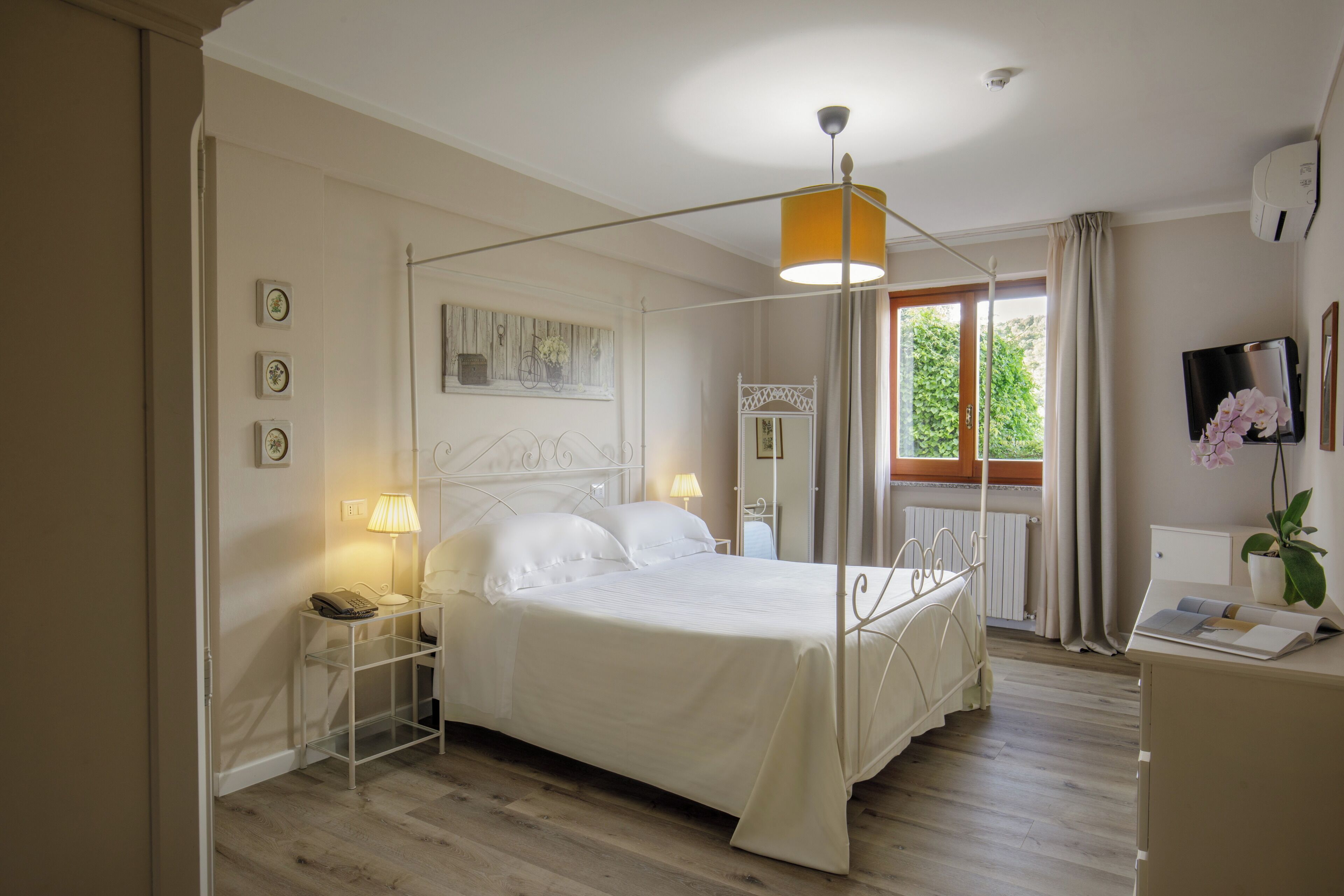 Een keurig opgemaakt slaapkamer met een hemelbed, nachtkastjes, een lamp en een raam met gordijnen.
