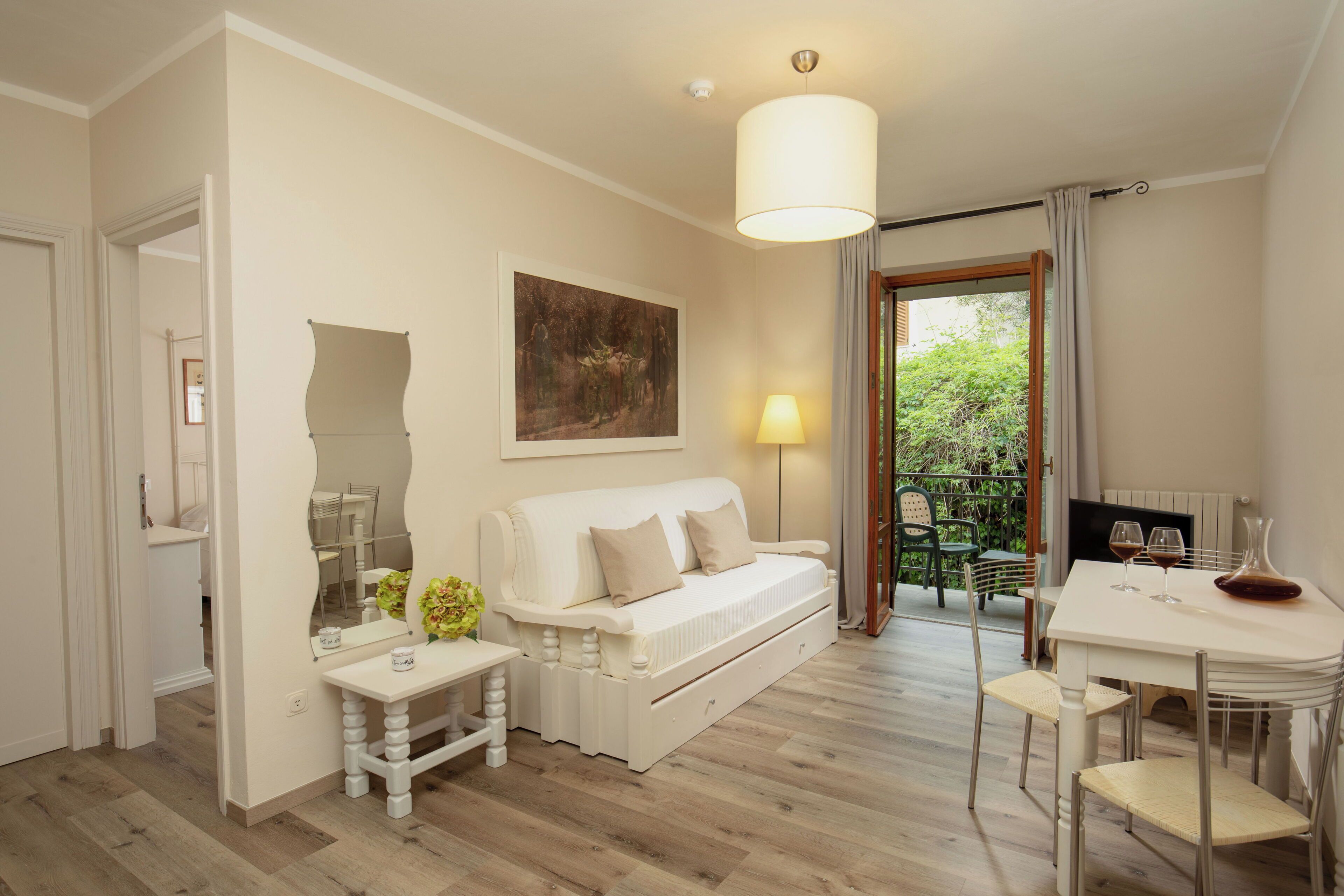 A cozy room with a white sofa, a dining table with chairs, a lamp, and a painting on the wall.