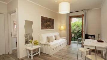 A cozy room with a white sofa, a dining table with chairs, a lamp, and a painting on the wall.