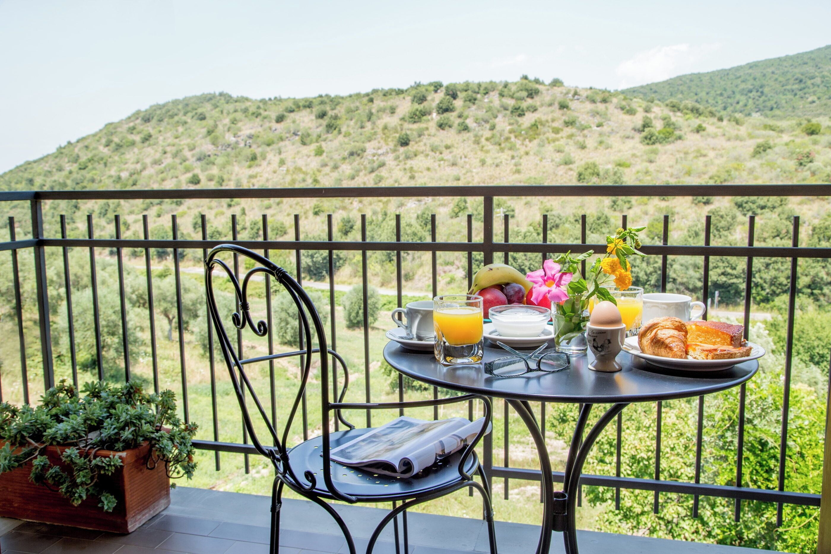 Ein Balkon mit einem Frühstückstisch, mit Croissants, Orangensaft und einer Vase mit Blumen.