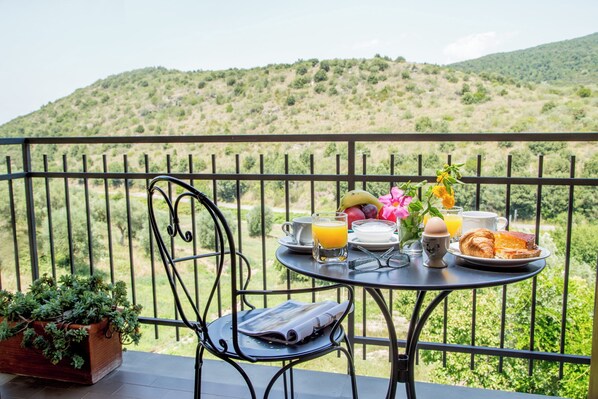A balcony with a table set for breakfast, including croissants, orange juice, and a vase with flowers.