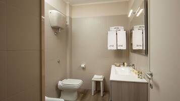 A modern bathroom with a toilet, sink, and a small stool. There are towels hanging on the wall and a mirror above the sink.