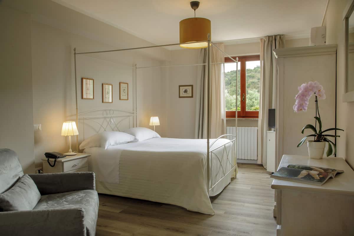 Ein Schlafzimmer mit Himmelbett, Nachttischlampen, einem Schreibtisch mit einer Zeitschrift, einem Topf-Orchideenstrauch und gerahmten Bildern an der Wand.