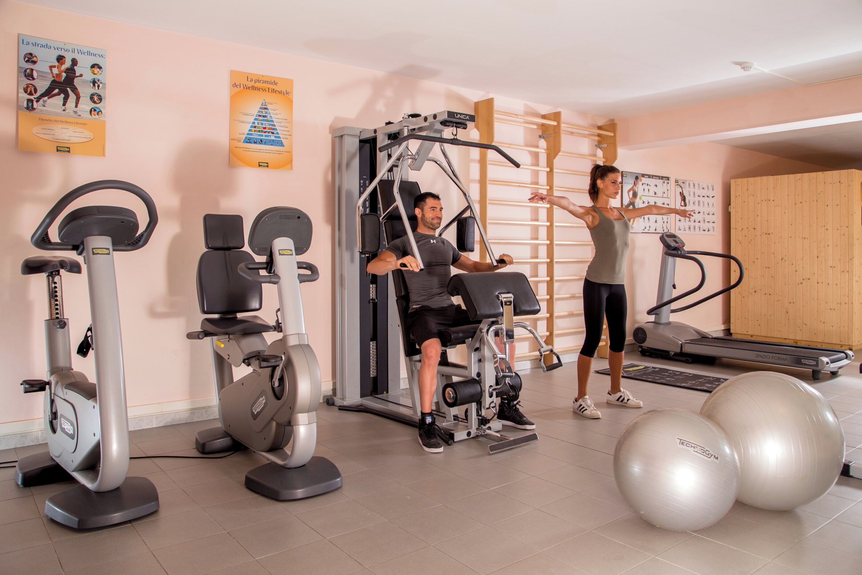 Ein Fitnessstudio mit Trainingsgeräten, darunter Laufband, Crosstrainer und Kraftgeräte.
