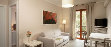 A modern living room with a sofa, a small table, a TV, and a window with curtains.