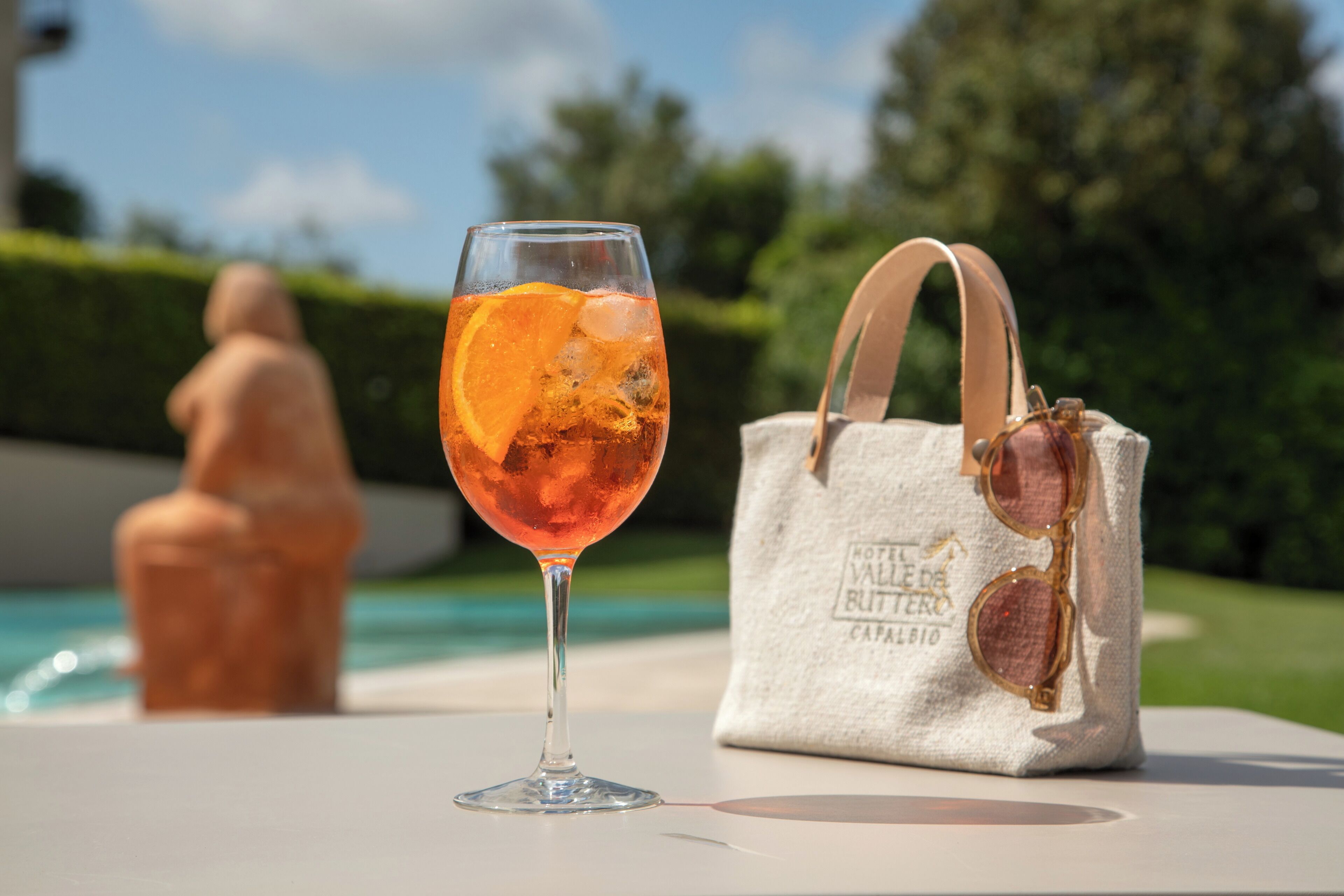 Ein Glas Orangensaft mit Eis, neben einer Stofftasche mit Sonnenbrillen und einem Logo.