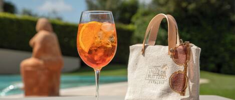 Un vaso de jugo de naranja con hielo junto a una bolsa de tela con gafas de sol y un logotipo.