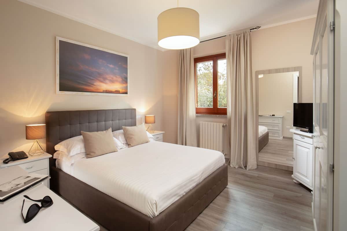 Ein modernes Hotelzimmer mit einem großen Bett, Nachttischlampen, einem Flachbildfernseher und einem Fenster mit Vorhängen.