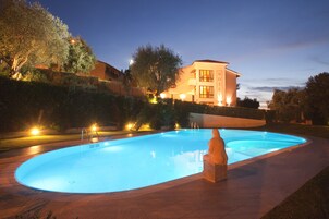 Una piscina con una estatua en el centro, rodeada de un patio bien iluminado.