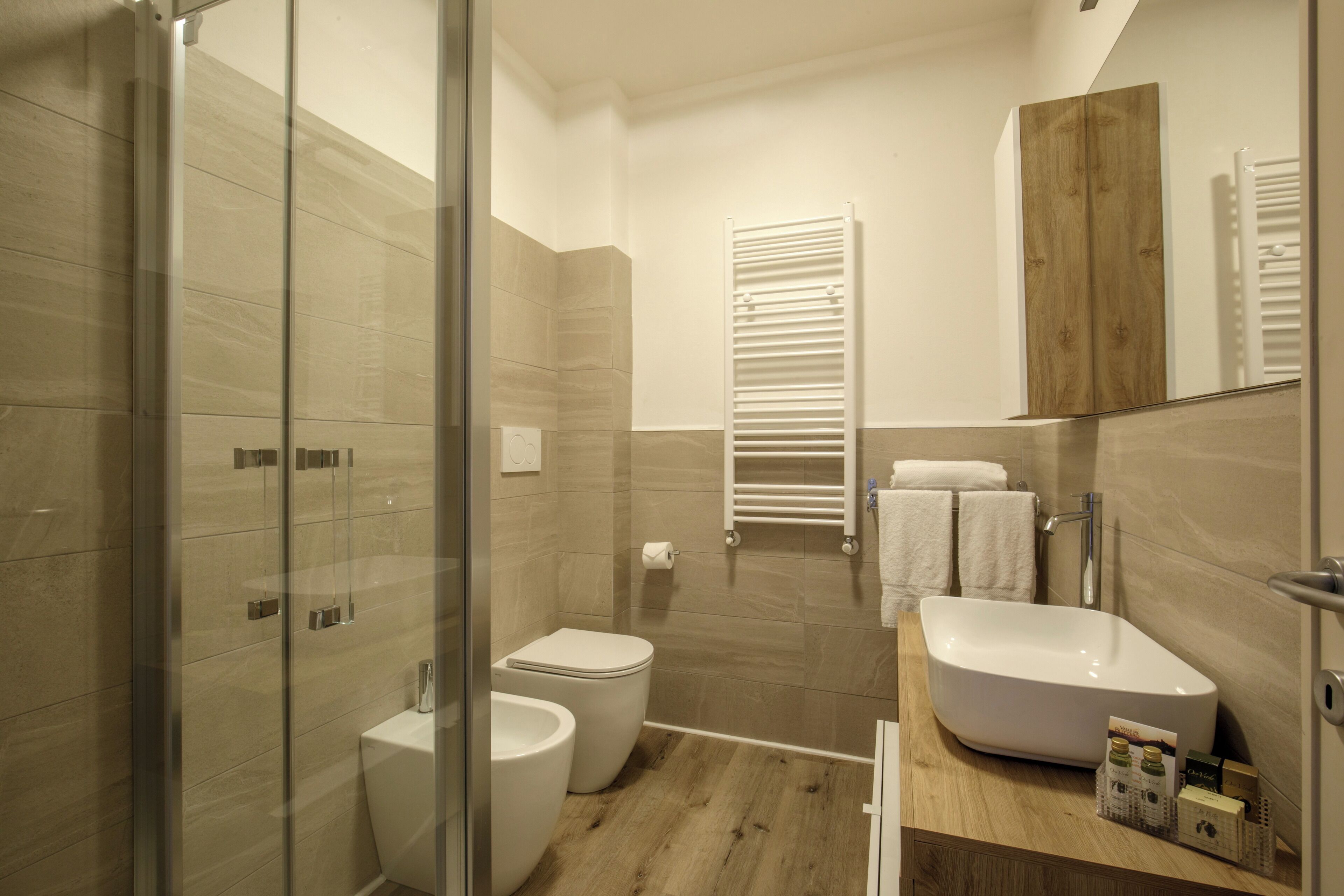Une salle de bain moderne dotée d’une douche à parois de verre, de toilettes sur pied, d’un bidet, d’un grand lavabo et d’un meuble-lavabo en bois.