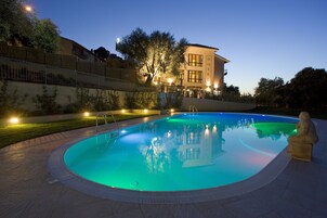 Una piscina con terraza de piedra, una estatua y un hotel al fondo.