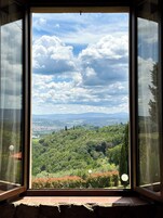 A window with a view of a lush green landscape, a clear sky, and distant mountains.