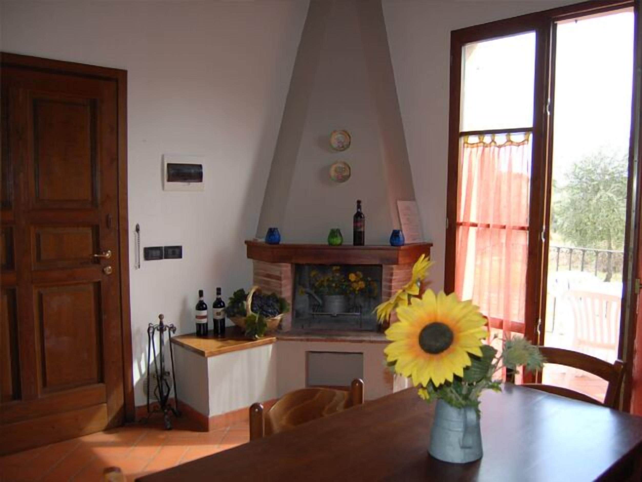 Un coin repas avec une table en bois, un vase rempli de tournesols et une cheminée agrémentée d’objets décoratifs.