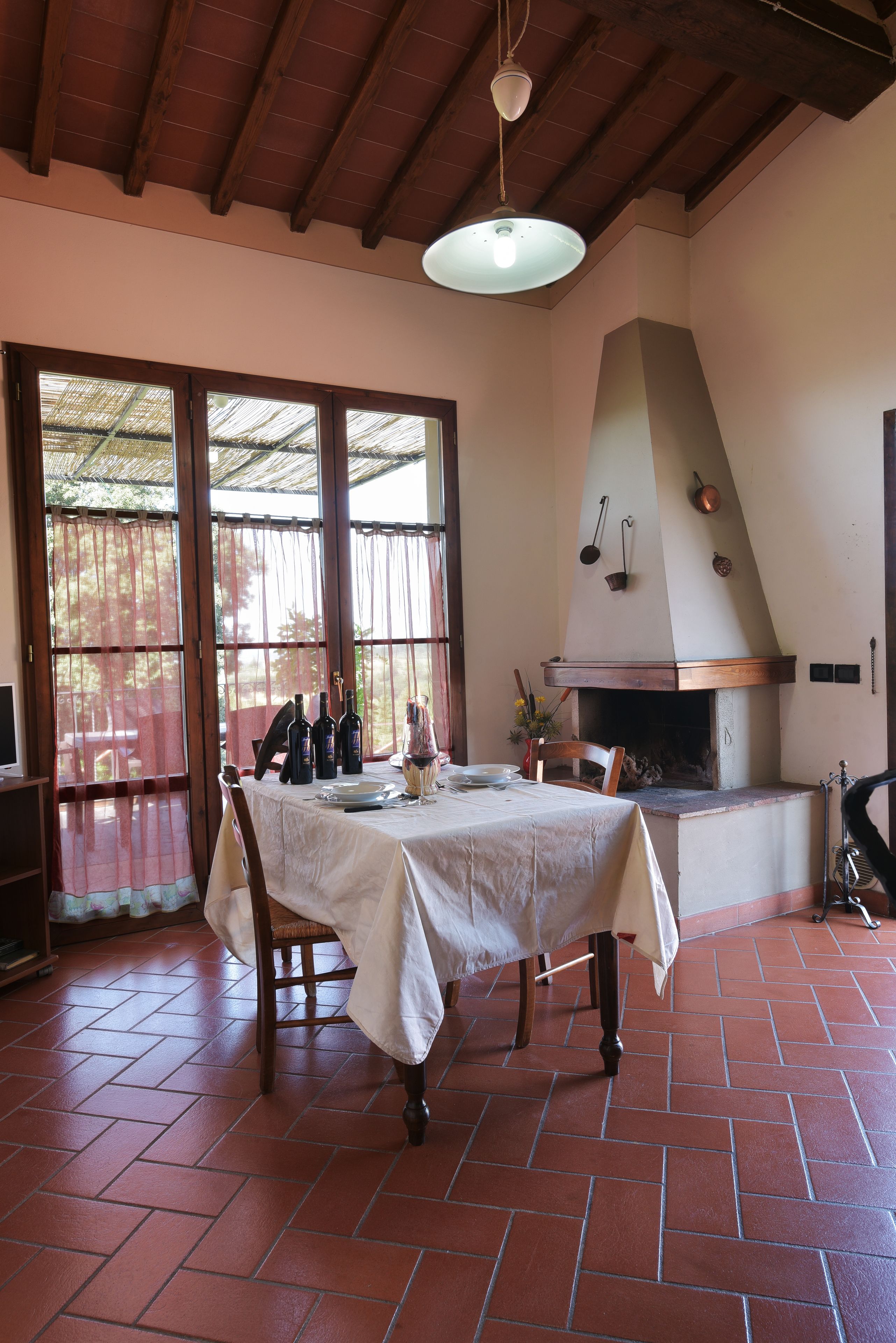 A dining area with a table set for two, a brick floor, and a wood-beamed ceiling.