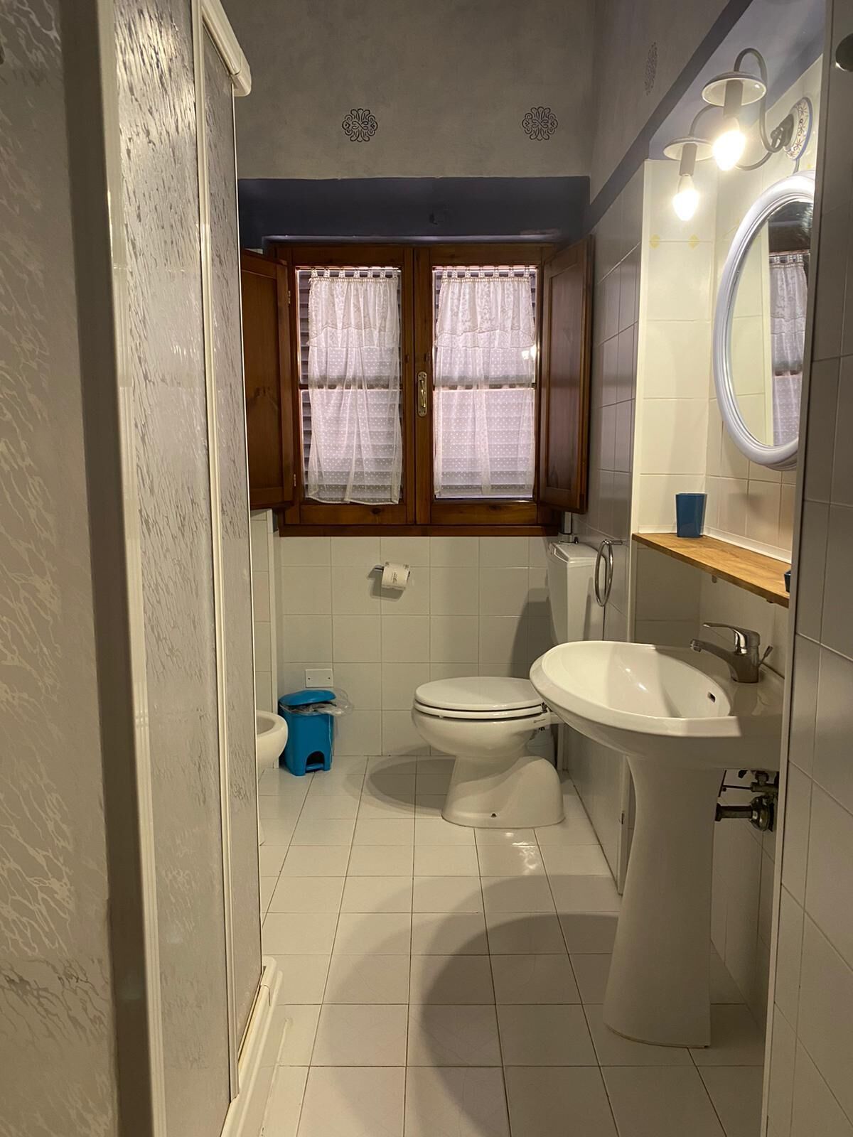 Un baño pequeño con inodoro, lavamanos y ventana con cortinas.
