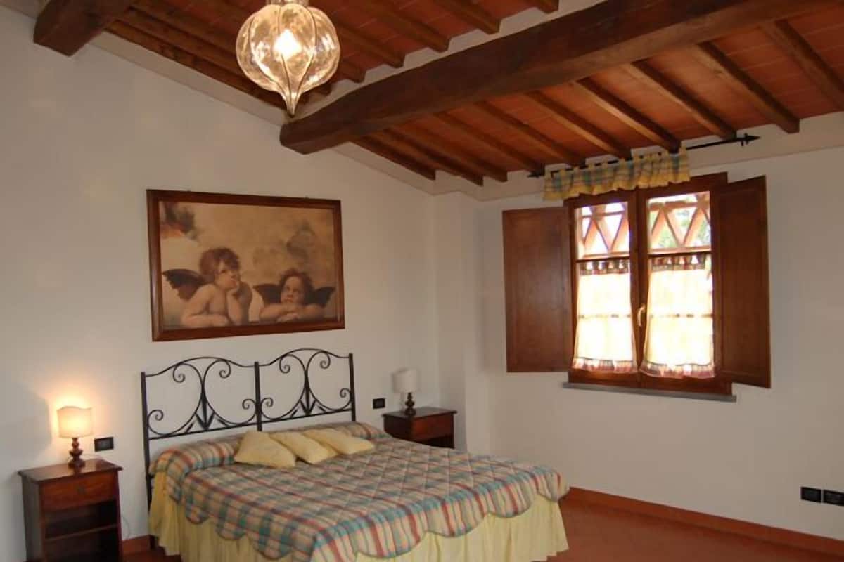 Un dormitorio con cama, un cuadro, una ventana con cortinas y un candelabro.