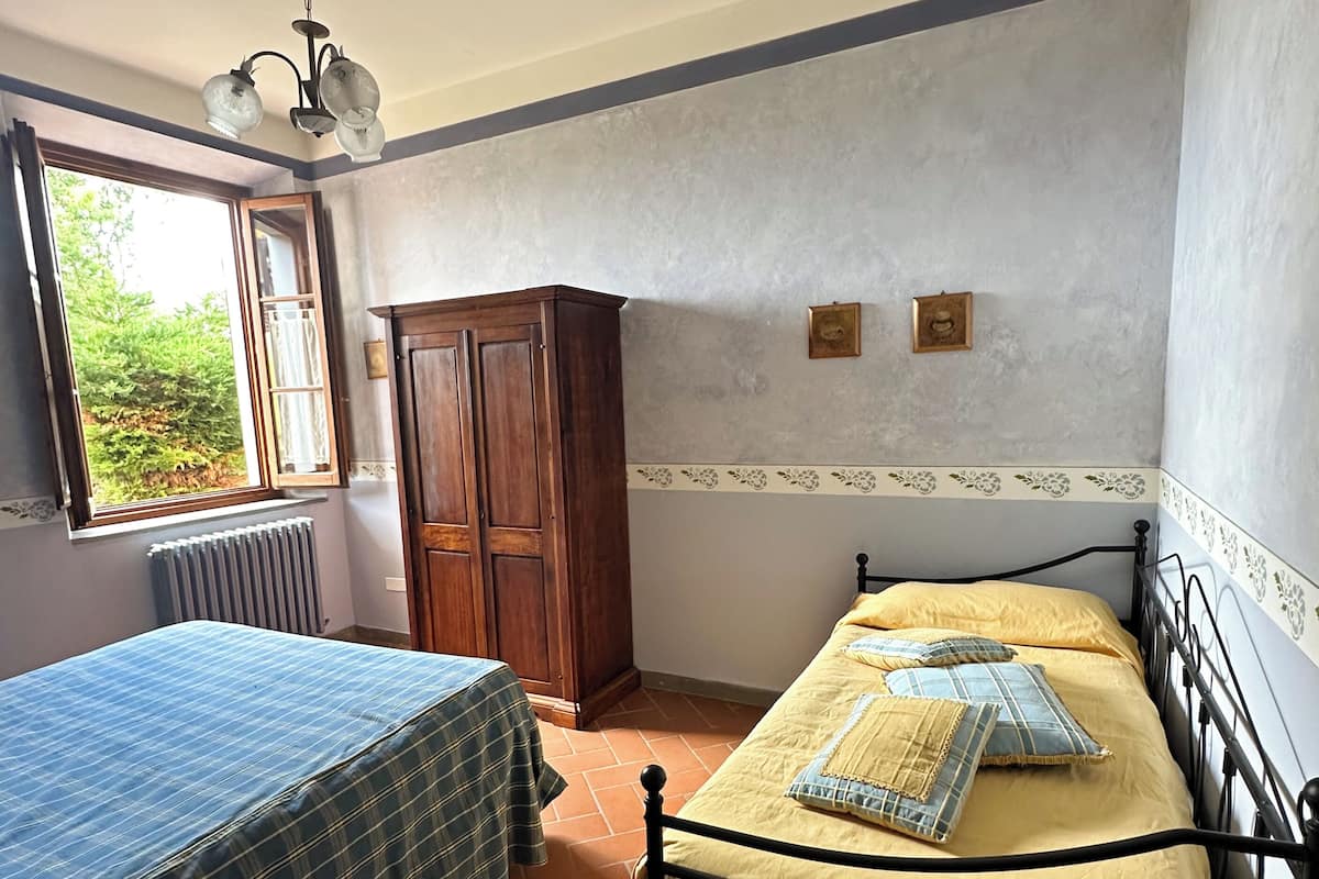 Un dormitorio con dos camas, un radiador, un armario y una ventana con vistas a zonas verdes.