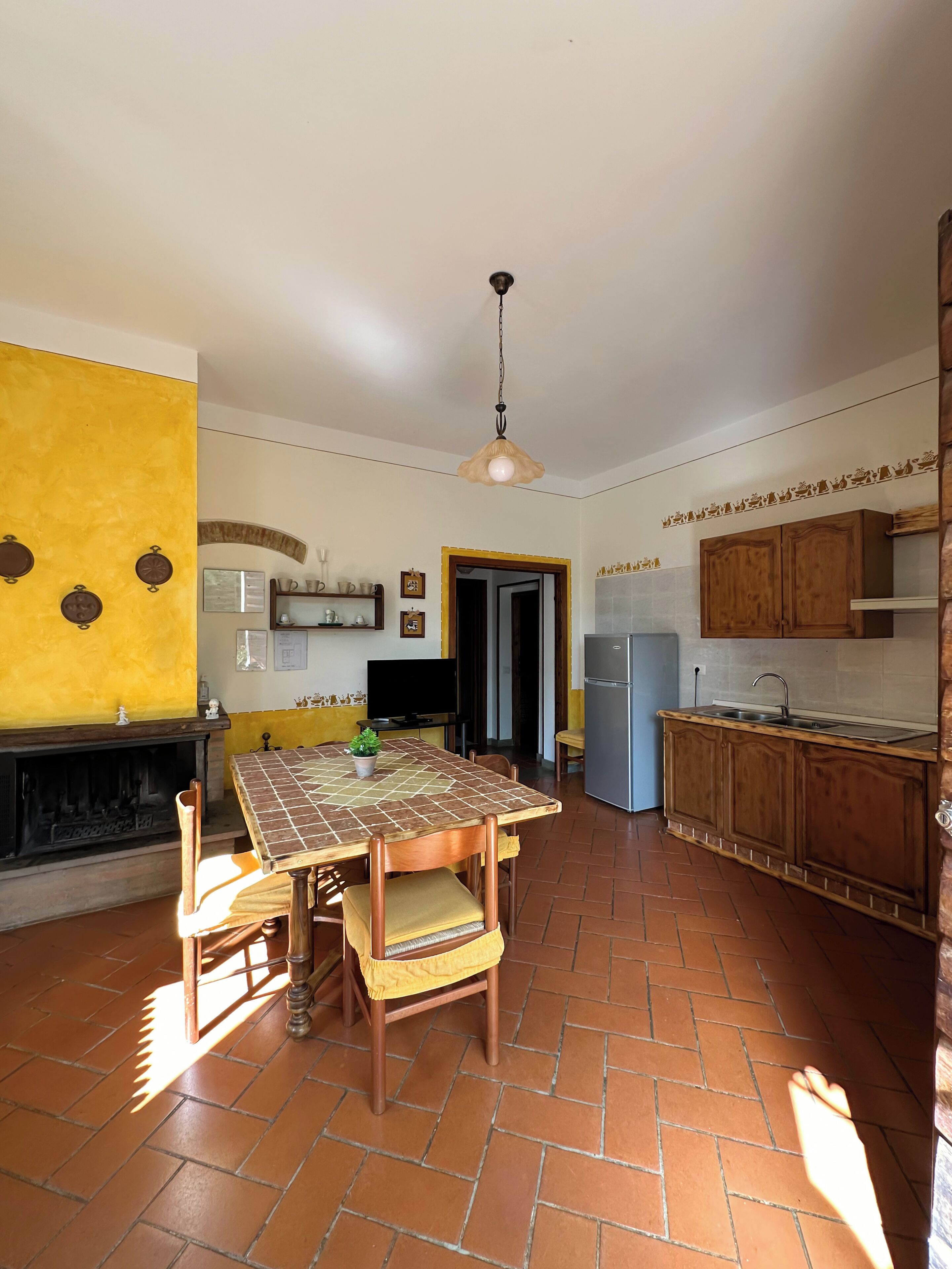 Een ruime keuken met betegelde vloer, houten keukenkastjes, en een eethoek met tafel en stoelen.