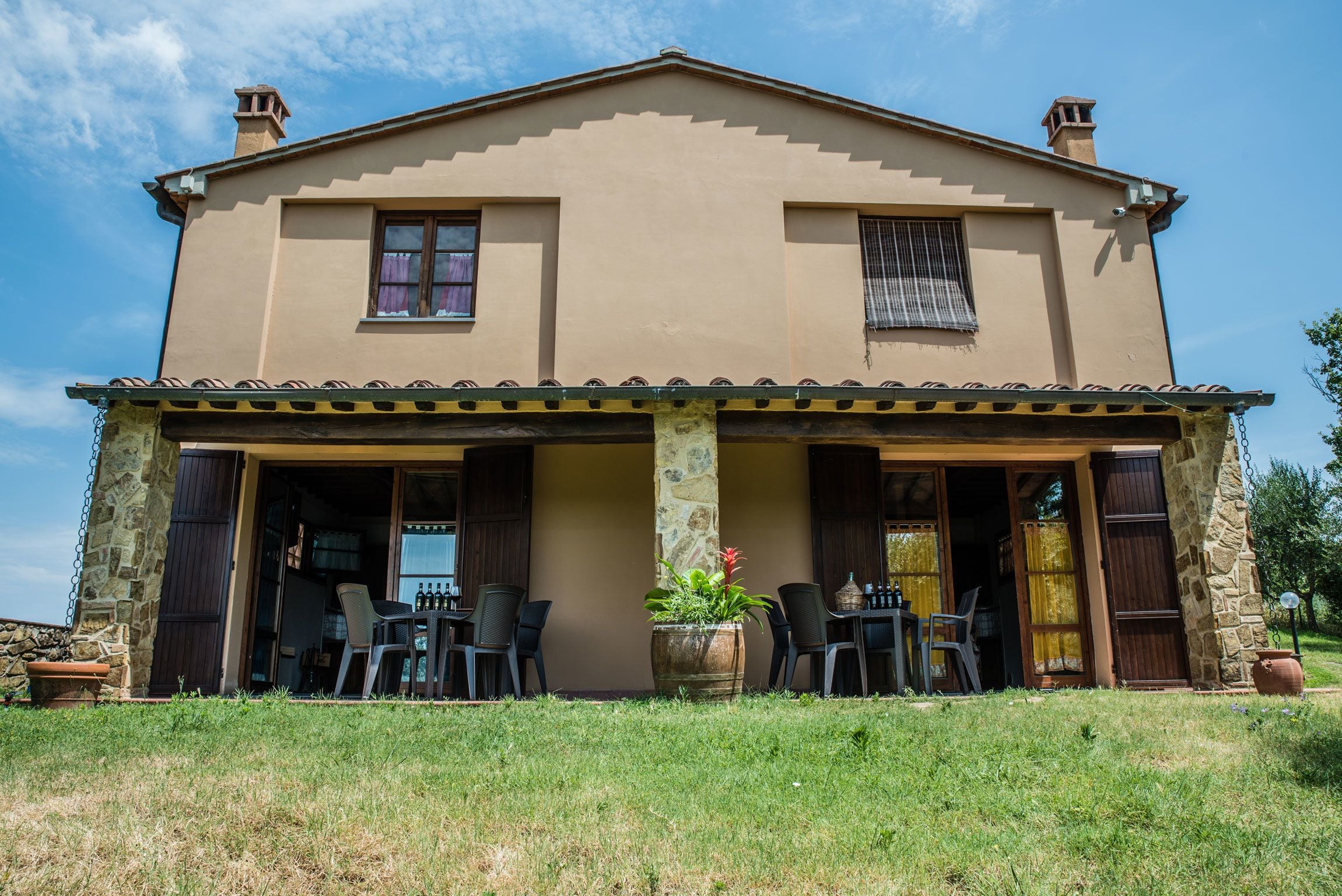 Une maison à deux étages dotée d’un patio couvert, de piliers en pierre et d’un jardin.