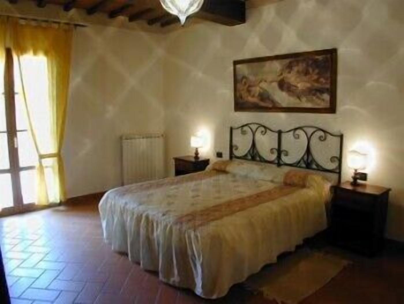 Un dormitorio con cama, dos mesitas de noche con lámparas, un radiador, una ventana con cortinas y un cuadro en la pared.